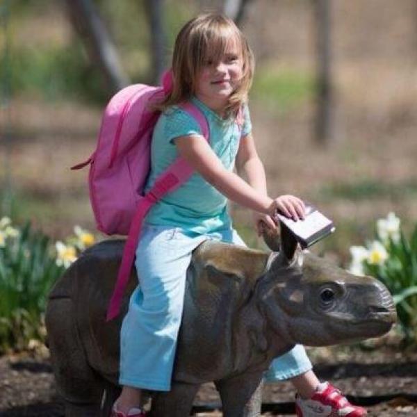 Girl with backpack riding rhino statue